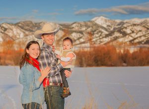 owner of High West Project Management Zac Davis posing with his wife and baby in front of the Bridger mountains in Montana