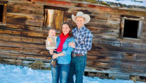 owner of High West Project Management Zac Davis with wife and baby posing outside in front of a rustic barn