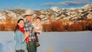 owner of High West Project Management Zac Davis posing with his wife and baby in front of the Bridger mountains in Montana