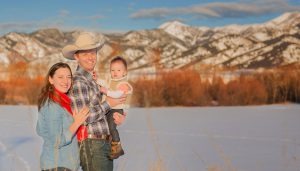 owner of High West Project Management Zac Davis posing with his wife and baby in front of the Bridger mountains in Montana