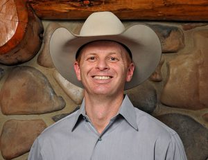 owner of High West Project Management Zac Davis is a button up shirt and cowboy hat smiling